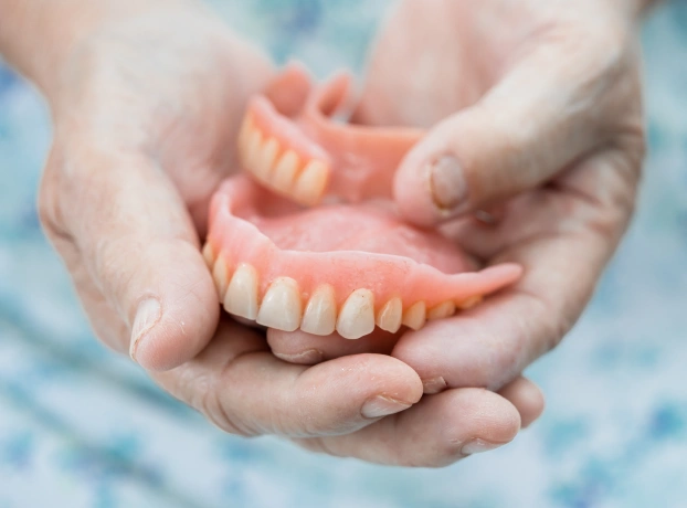 Hands holding a full set of upper and lower pink dentures
