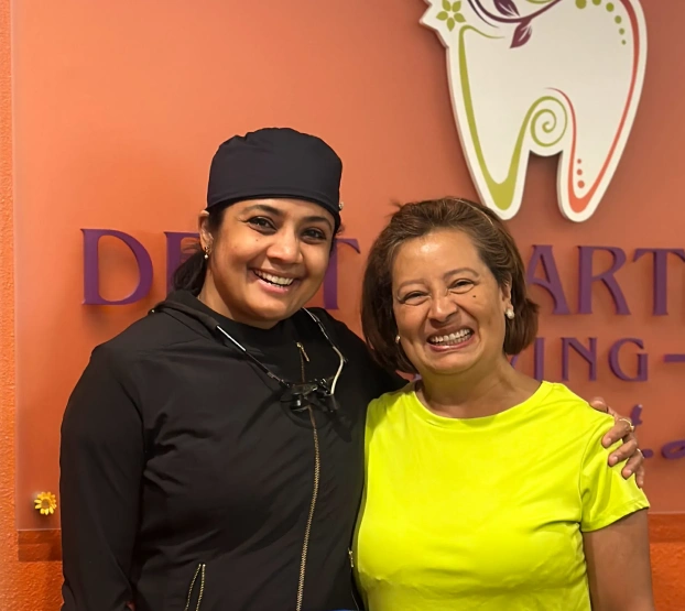 Dr. Radhika Srikrishnan Iyer posing with a patient in front of the Dental Artistry Irving sign