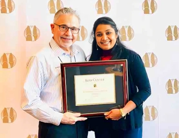 Two people posing together holding a framed certificate