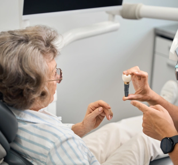 Dental professional showing a dental implant model to an older female patient in a dental chair