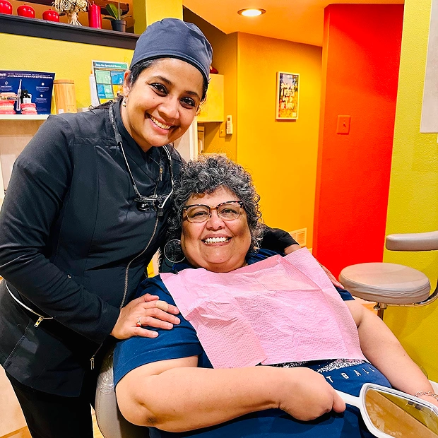 Dr. Radhika Srikrishnan Iyer in a surgical cap posing with an older female patient in a dental chair